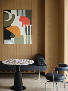 A minimalist interior featuring a wooden bench, marble table, and a black leather chair.