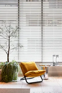 A modern living room featuring a yellow velvet chair with metallic legs, a sleek metallic side table, and a plant.