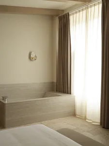 A modern, minimalist bedroom featuring a concrete bathtub and floor-to-ceiling curtains.