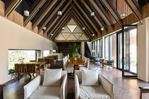 Modern restaurant interior with a high ceiling, wooden beams, and a mix of seating arrangements.