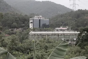 一座現代辦公大樓，擁有玻璃窗與混凝土柱，周圍環繞茂密綠意，坐落於丘陵地形上。