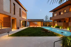 A modern residential building with a concrete exterior and a courtyard with a pool and greenery at dusk.