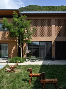 A modern residential exterior featuring wood and concrete materials surrounded by nature.