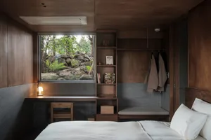 A minimalist bedroom featuring a wooden kitchenette with a view of the outdoors.