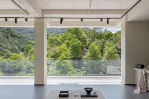 A modern living room with a large glass window overlooking lush greenery and mountains.