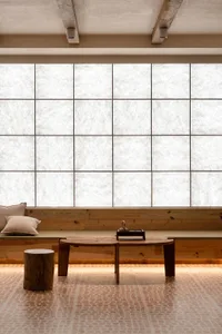 A minimalist living space featuring a large window with wood frames and a wooden table with a teapot and cup.