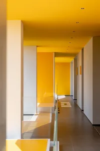 A modern corridor featuring yellow walls, white pillars, and glass railings.