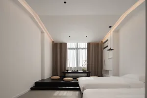 A minimalist bedroom with white walls and furniture, featuring a low platform with a table and cushions.