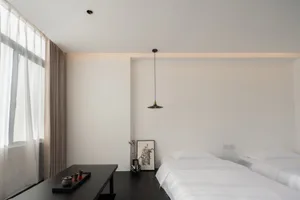 A minimalist residential room with white walls, dark wood accents, and sheer curtains.