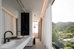 A minimalist bathroom with glass walls, concrete floor, and textile window treatments.