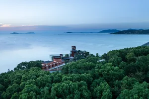 Lush green forest along a calm beach with a modern architectural structure in the foreground.