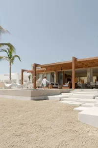 A beachfront resort with concrete and wooden structures, featuring a walkway and outdoor seating.