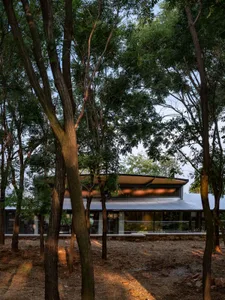 A modern residential extension with a metal roof and large glass windows surrounded by trees.