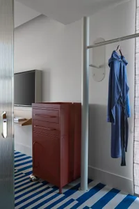 A minimalist bedroom featuring a red metal cabinet on wheels and a blue and white striped rug.
