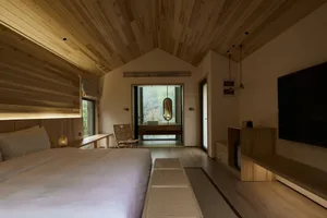 A minimalist bedroom featuring wooden furniture and a large window with a view of nature.
