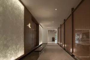 A minimalist corridor with wooden walls and paper screens, leading to a bright area with concrete flooring.