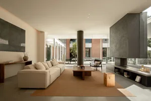 A minimalist living room with concrete walls, floor, and furniture, featuring a large beige sofa, a wooden coffee table, and 