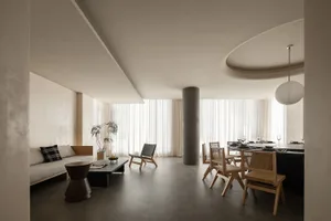 A minimalist living space featuring a concrete floor and walls, with a large sofa, chairs, and a dining table.