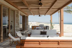 A minimalist residential exterior featuring wood, stone, and glass materials with a beachfront view.
