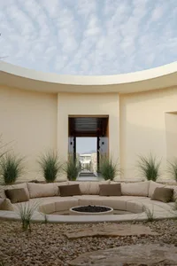 A modern architectural exterior featuring a circular, concrete space with seating and a fire pit.