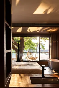 A modern bedroom with a balcony featuring wooden furniture, glass walls, and concrete elements.