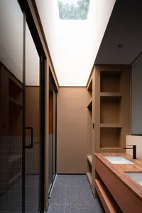 A modern bathroom interior with concrete and tiled surfaces, featuring a long countertop with built-in shelves and a skylight