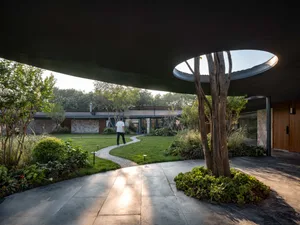 A modern garden with a concrete path winding through the greenery and a person walking on it.