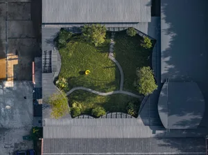 A modern, green garden with a yellow sculpture and a curved path surrounded by buildings.