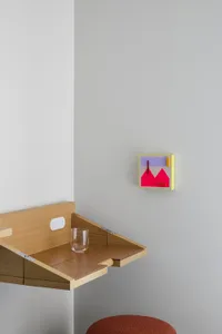 A minimalist home office space featuring a wooden desk with a glass surface, a glass tumbler, and a colorful abstract wall ar