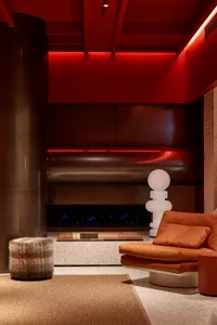 A modern living room with concrete walls, a leather sofa, and a fireplace with red lighting.