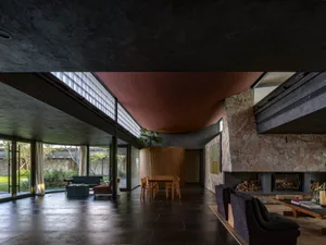 Modern living room with stone and wood finishes, featuring dark concrete ceiling and large windows.