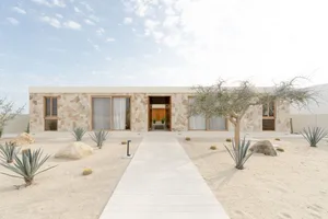 A modern minimalist residential house with a flat roof and large windows, constructed from sandstone and featuring cactus and