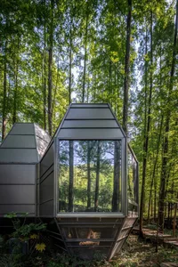 A modern modular house with metallic and glass elements in a forested setting.