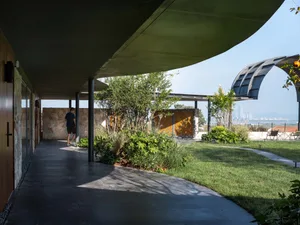 A modern residential patio featuring concrete, metal structures, lush green grass, and various plants