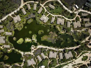 Aerial view of a residential lot with houses surrounded by greenery and water features.
