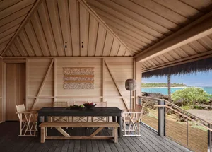A wooden patio table with chairs and rug, ocean view outdoors.