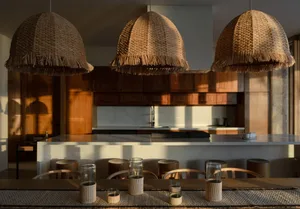 A modern kitchen featuring natural fiber lighting fixtures and wooden stools.