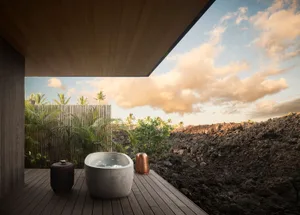 Modern outdoor bathroom with a wooden deck, concrete bathtub, and a view of a rocky landscape with greenery and clouds in the