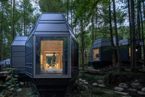 Modern treehouse hotel with glass walls and metal structure amidst a forest setting.