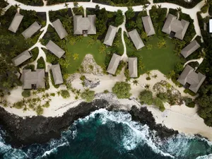 Aerial view of residential beachfront houses with palm trees and sand.