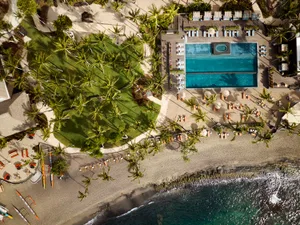 Aerial view of a vacation resort with a pool, beach, and palm trees.