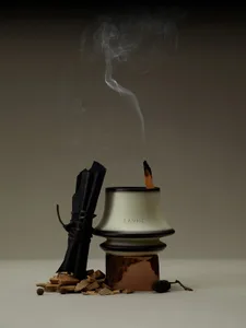An industrial-style incense burner made of metal with a smoking stick inside, surrounded by wood chips and drier.