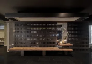 A minimalist lobby with wooden benches and concrete panels, featuring a Zen-inspired arrangement with a vase and candles.