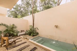 A serene outdoor space featuring a concrete pool surrounded by gravel, with various plants and a wooden deck chair.