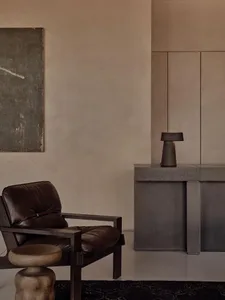 A minimalist living room with a dark leather armchair, a concrete side table with a lamp, and a large abstract painting on th