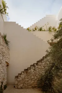 Concrete stairs leading upwards, surrounded by greenery and white walls.