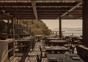 Well-dressed tables in a wooden restaurant setting overlooking the ocean.