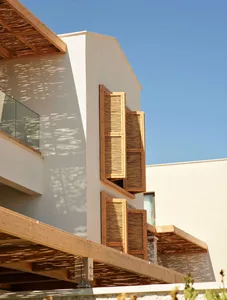Modern building exterior featuring wooden shutters and balconies with sunlit shadows.
