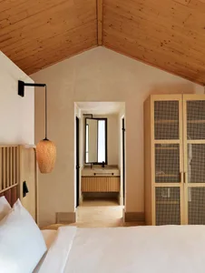 A minimalist bedroom featuring a bed with a wooden headboard, a hanging wicker pendant light, and a wooden closet with a grid