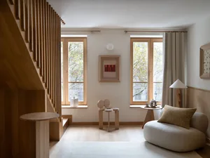 A minimalist living room with wooden elements, featuring a soft couch, a wooden table, and a set of wooden stools against a n
